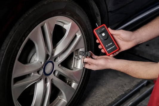 TPMS reset vs relearn vs programming: a KINGBOLEN EL-50448 TPMS tool activating a sensor at a silver alloy wheel