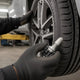 TPMS sensor replacement cost: mechanic holding a new TPMS sensor next to a wheel on a lift